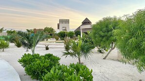 A resort with a pool, palm trees, and a building with a thatched roof.