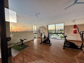 Um quarto espaçoso com uma grande janela, piso de madeira e várias bicicletas de exercício.