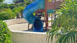A play structure with a slide and a wooden building with a thatched roof.