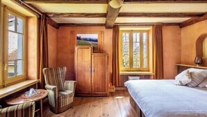 A room with a bed, a chair, a small table, a wardrobe, and a window with a view of the outdoors. - Goute la vie  (Marchamp)