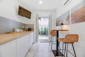 Una cucina piccola con un piano di lavoro in legno, una televisione montata sopra e un'area pranzo con due sedie in vimini e un tavolo.