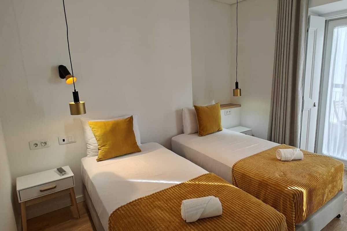Une chambre d’hôtel avec deux lits, un petit bureau et une fenêtre avec des rideaux.