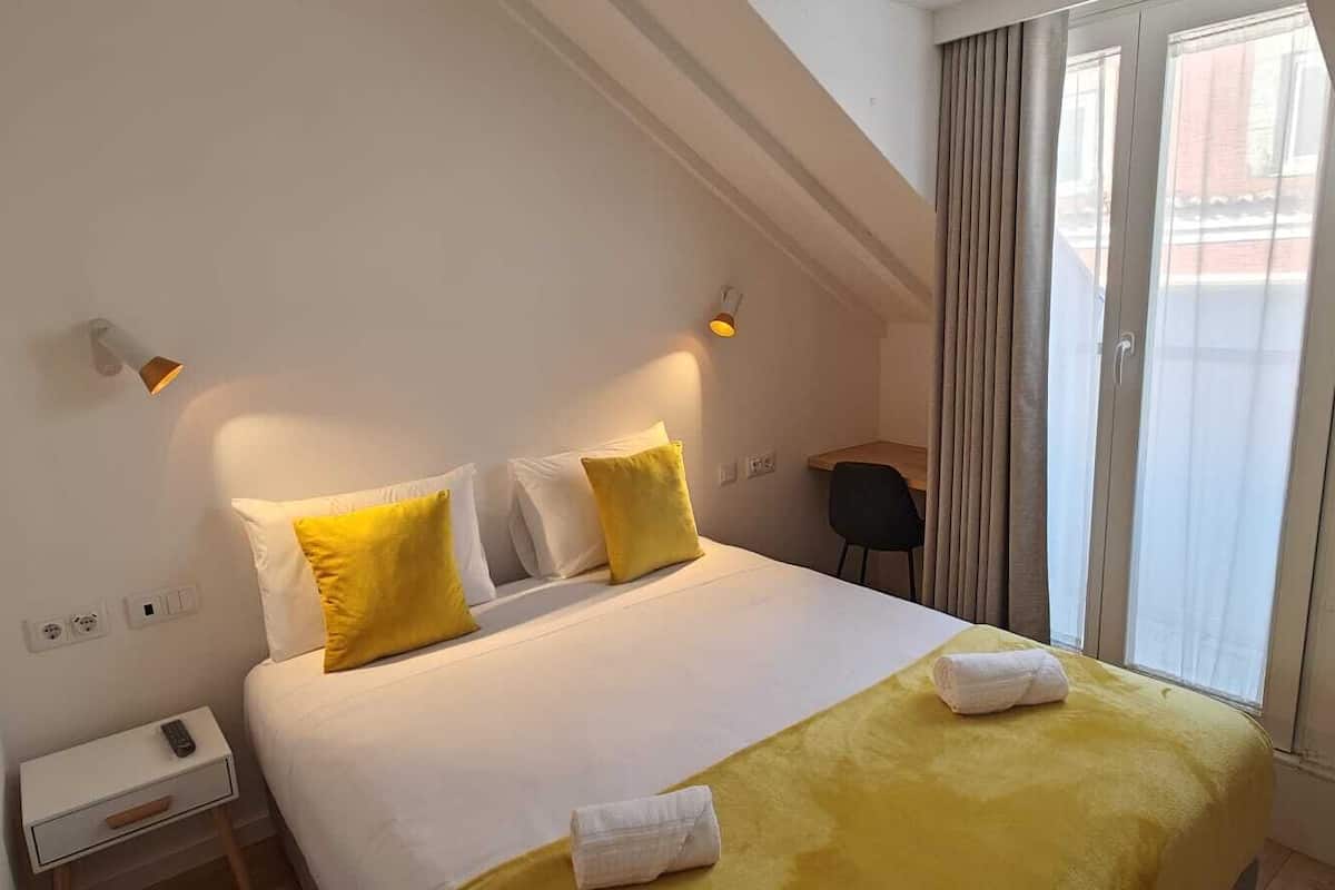 Une chambre d’hôtel avec un lit, un bureau, une chaise et une fenêtre avec des rideaux.