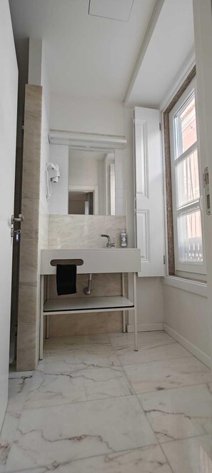 A modern bathroom with a marble floor, a white sink, and a large mirror.