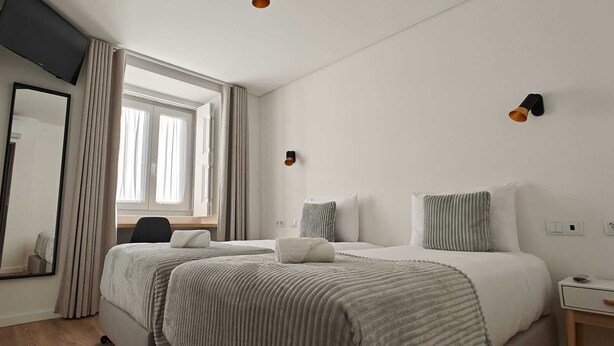 Een hotelkamer met een bed, een bureau, een stoel, een spiegel en een raam met gordijnen.