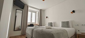 A hotel room with a bed, a desk, a chair, a mirror, and a window with curtains.