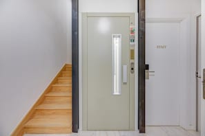 L’entrée d’un hôtel, avec un escalier en bois, une porte dotée d’un luminaire et une enseigne indiquant « PERSONNEL ».