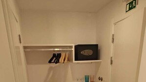 Een kleine kamer met een inbouwed bed, een klein plankje met een speaker en een deur met een nooduitgangbord.