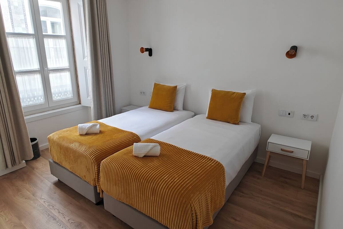 Une chambre d’hôtel avec deux lits, une petite table de chevet, un miroir et une fenêtre avec des rideaux.