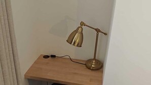 Een hoekappartement met een houten bureau, een zwarte stoel, een messing bureaulamp en een blauw vloerkleed.