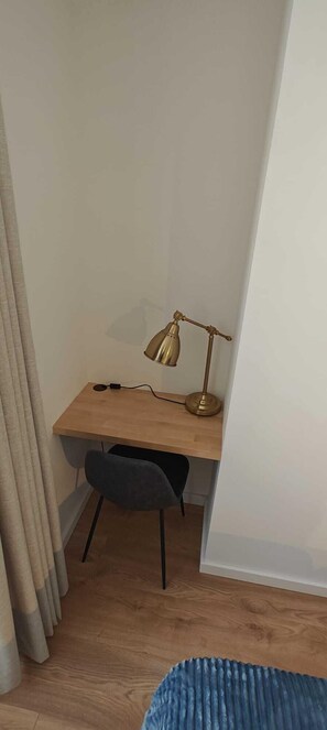 A corner room with a wooden desk, a black chair, a brass desk lamp, and a blue rug.