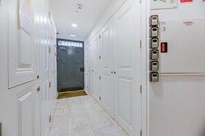A hotel corridor with white doors, a grey door at the end, and a wall-mounted elevator control panel. -  Correio Velho Hotel (Lisbon)