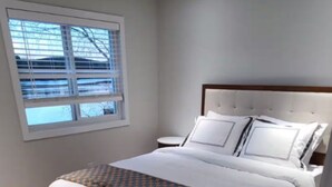 A bedroom with a large bed, a nightstand, and a window with blinds.