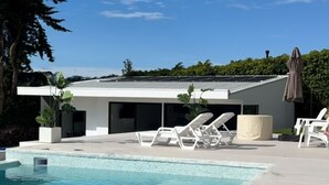 A modern house with a swimming pool, white lounge chairs, and a covered patio area.