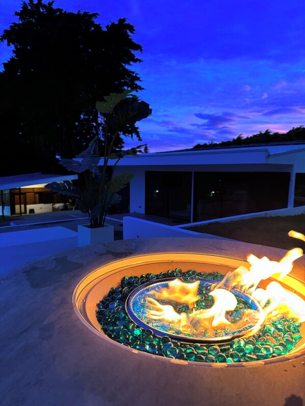 A fire feature with glass pebbles, surrounded by a concrete border, in an outdoor setting.
