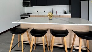 A modern kitchen with a central island, black bar stools, and pendant lighting.
