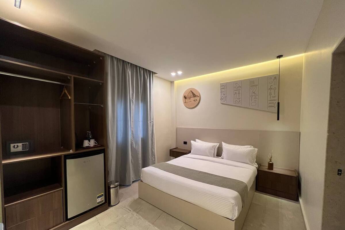A modern hotel room with a bed, bedside tables, a wardrobe, and a small refrigerator.