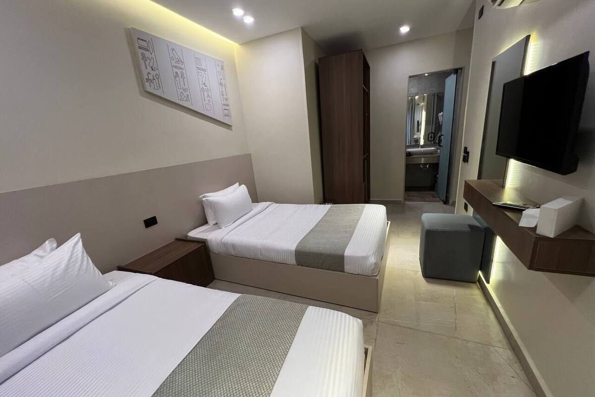 A hotel room with two beds, a TV, a desk, and a bathroom visible in the background.