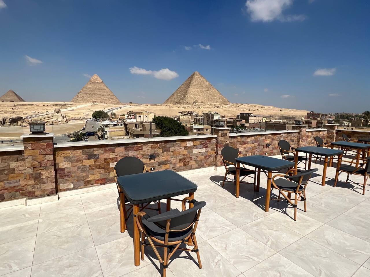 Terraza al aire libre con muros de piedra, mesas y sillas, con vista a las pirámides.