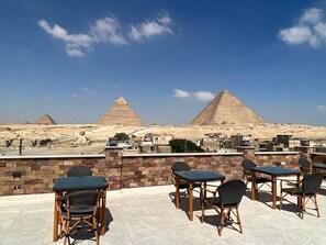 A rooftop terrace with tables and chairs, offering a view of the pyramids. - Pyramids Island (Giza)