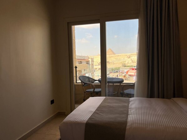 Habitación de hotel con cama, una silla, una mesa y vista a una pirámide.