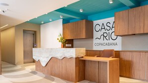 A reception desk with a wooden finish, a white counter, and a sign reading "CASA RIC COPACABANA".
