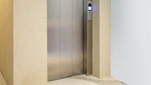 A modern elevator with a control panel, set in a minimalist interior with plain walls and a light-colored floor.