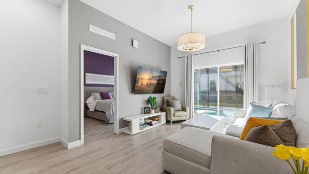 A modern living room with a sofa, coffee table, and a TV. There is a balcony with a view of the outdoors. - Serenity Townhouse! Private Pool and Pet-Friendly (Davenport)