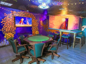 A room with a round table, chairs, a television, and a wall decorated with flowers.