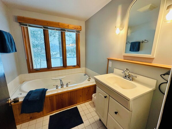 A bathroom with a wooden bathtub, a white sink, and a window with a view of trees.