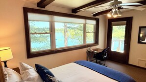 A bedroom with a large bed, a desk, and a view of a lake. - Beautiful Lakefront cabin woodburning fireplace, grill, canoe, SUP, AC, parking. (Wautoma)