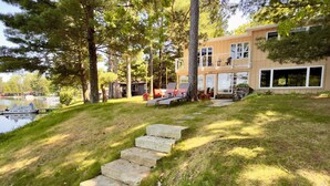 A two-story building with a stone staircase leading up to a deck area. - Beautiful Lakefront cabin woodburning fireplace, grill, canoe, SUP, AC, parking. (Wautoma)