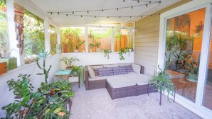 Un porche cubierto con un sofá de mimbre, plantas en macetas y luces colgantes.