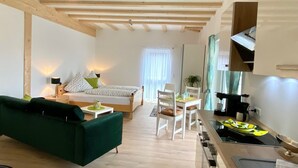 A modern living room with a green sofa, a dining area with white chairs, and a kitchen with a stove. - Schönes helles Studio-Appartement mit großem Balkon (Engelsbrand)