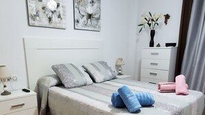 Un dormitorio ordenado con cama, almohadas, mesita de noche, cómoda y una obra de arte en la pared.