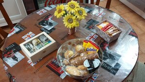 Una mesa redonda con superficie de vidrio, decorada con elementos temáticos británicos, incluyendo un jarrón de girasoles, una cesta de galletas y una caja de cola.