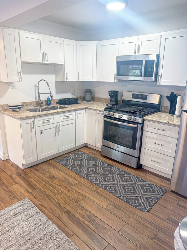 Een moderne keuken met witte kasten, roestvrijstalen apparatuur en een vloerkleed met een herringbone-patroon.