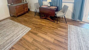 Een kamer met een houten vloer, een eettafel met stoelen, een kast en een raam met blauwe gordijnen.