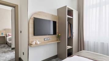 Une chambre d’hôtel équipée d’un téléviseur fixé au mur, d’une étagère en bois agrémentée d’objets décoratifs, d’une armoire et d’un lit.