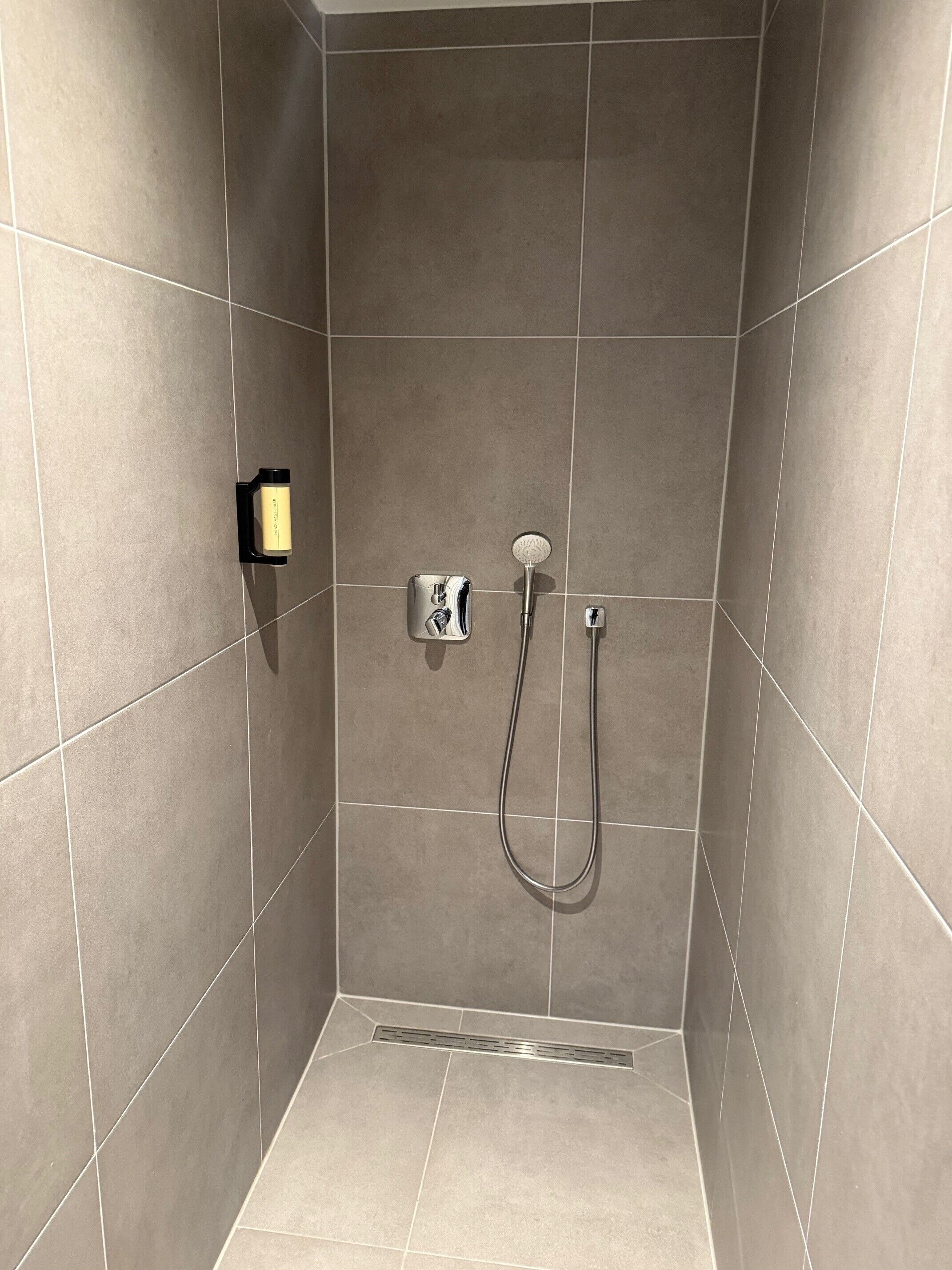 Un espacio de ducha con paredes de azulejos, un cabezal de ducha manual y un panel de control.