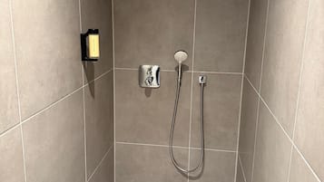 Un espacio de ducha con paredes de azulejos, un cabezal de ducha manual y un panel de control.