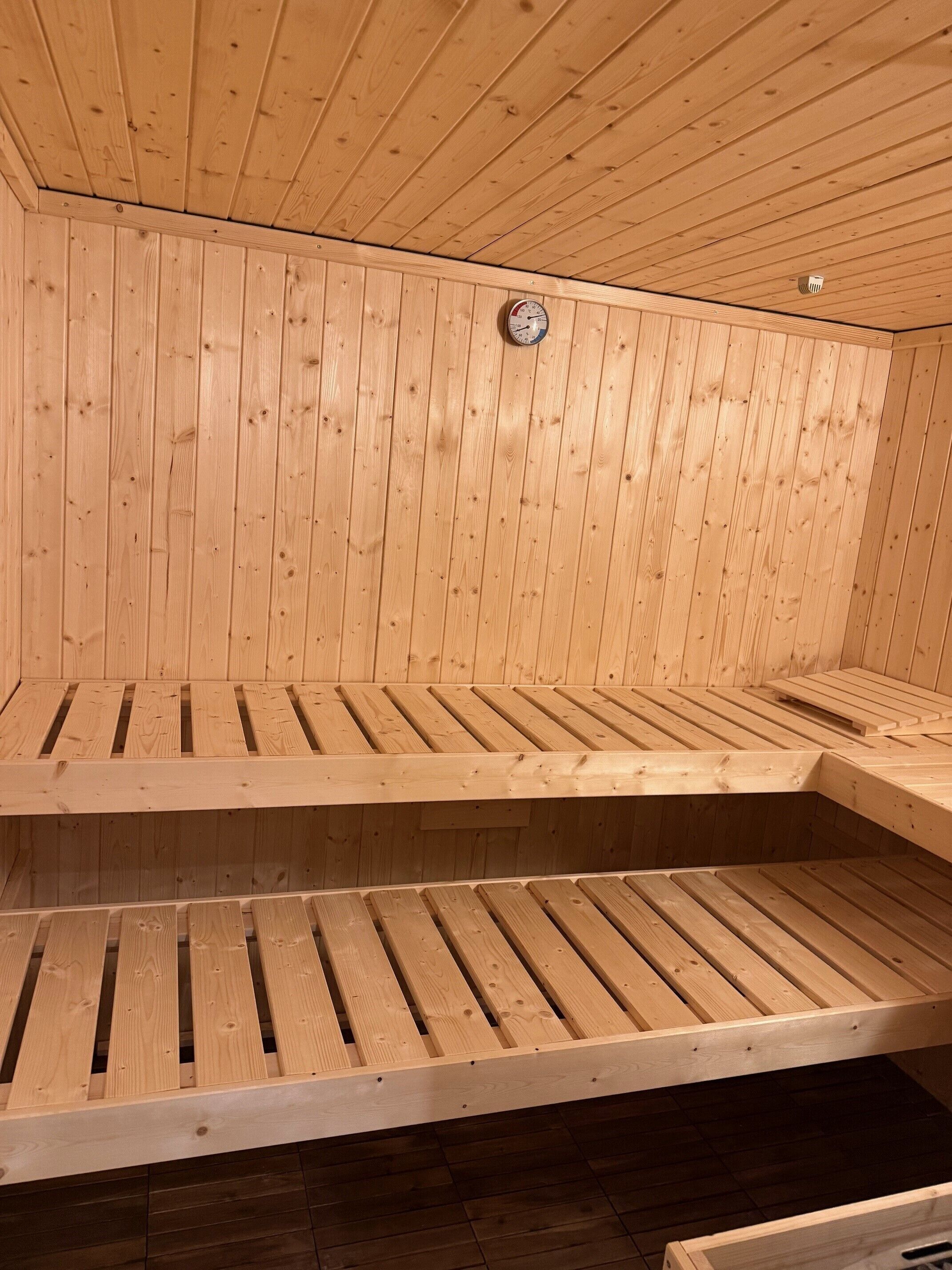 Eine Sauna mit Holzbänken und einem sichtbaren Temperaturanzeiger an der Wand.