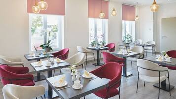 A modern dining area with tables and chairs, large windows, and hanging pendant lights.