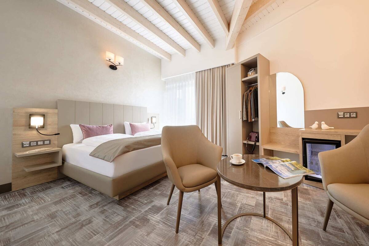 Hotelkamer met een bed, twee fauteuils, een tafeltje, nachtkastje, spiegel, kast en een open haard.
