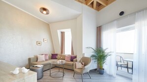 Una sala moderna con un sofá modular, una mesa redonda, una silla y una planta en maceta. Tiene un balcón con vistas.