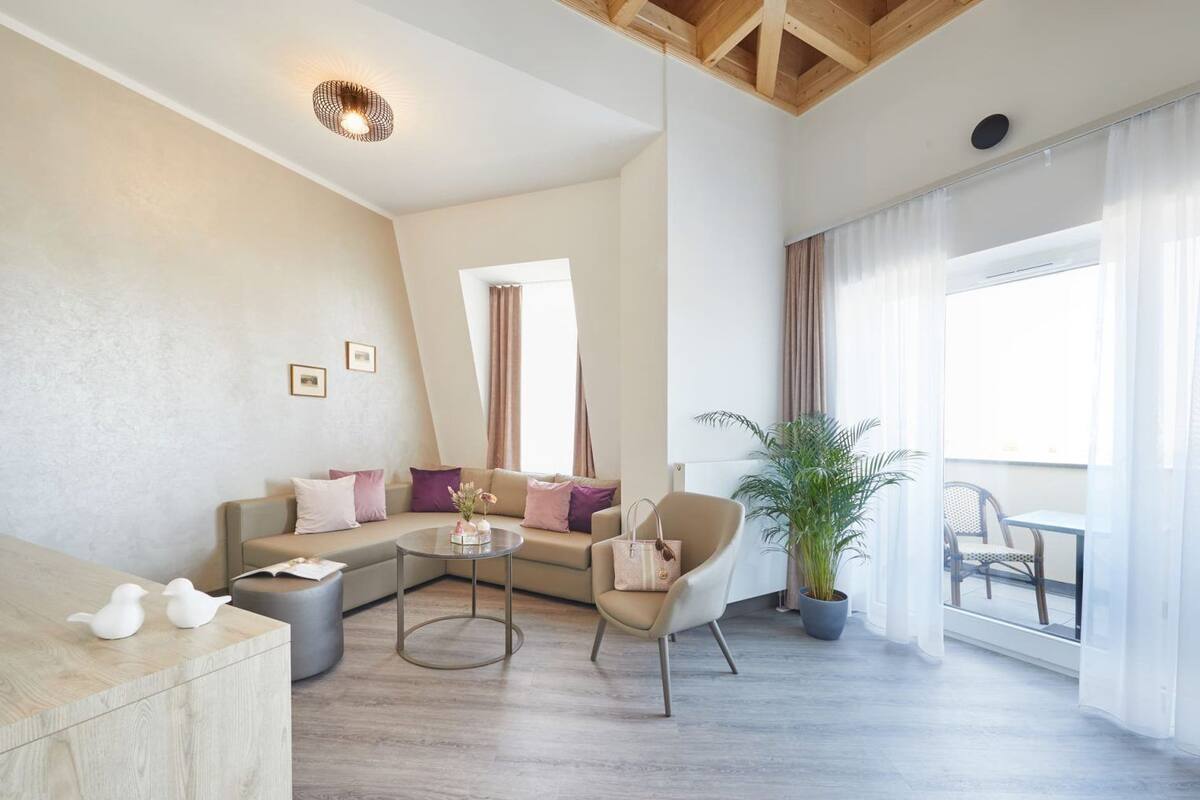 Een moderne woonkamer met een modulaire bank, een ronde salontafel, een fauteuil en een potplant. Er is een balkon met uitzicht.