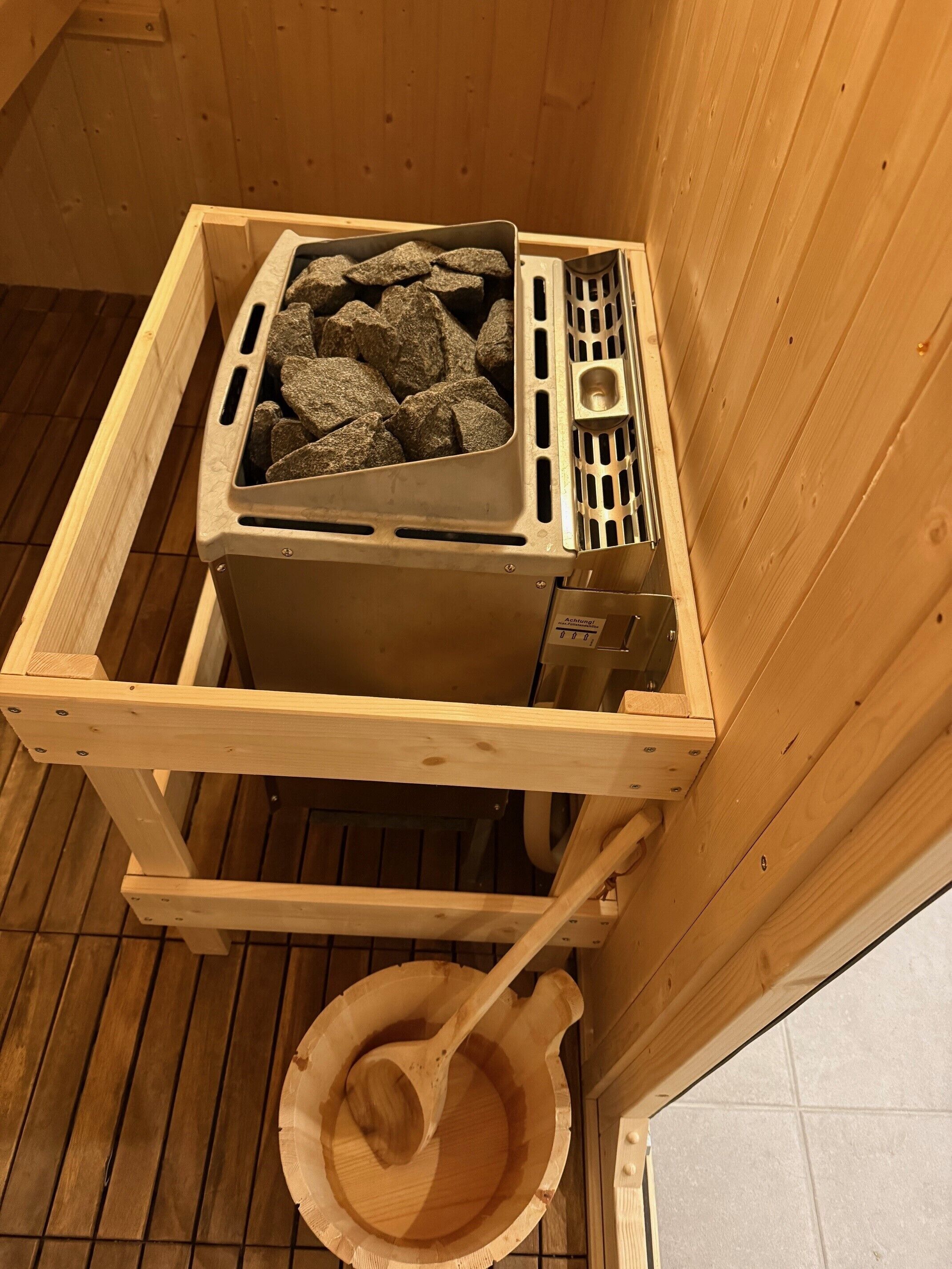 Eine Sauna mit Holzbank, einem mit Steinen gefüllten Behälter und einem Holzkochlöffel.
