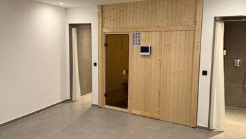 Een ruime kamer met een houten scheidingswand, een schuifdeur en een klein zitgedeelte met een bank en kussens.