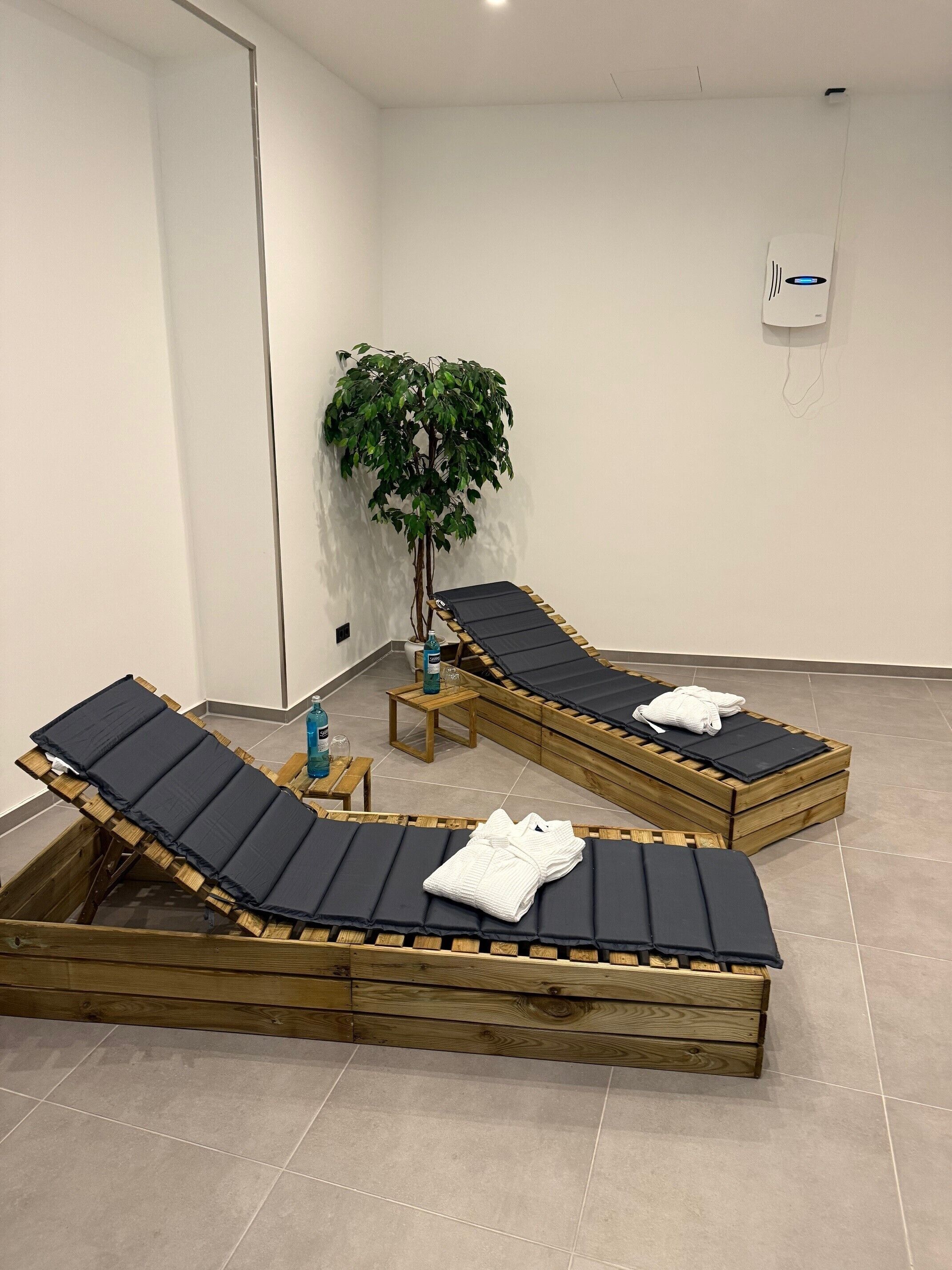 Una habitación con dos sillones de madera, una mesita, una planta y un dispositivo montado en la pared.