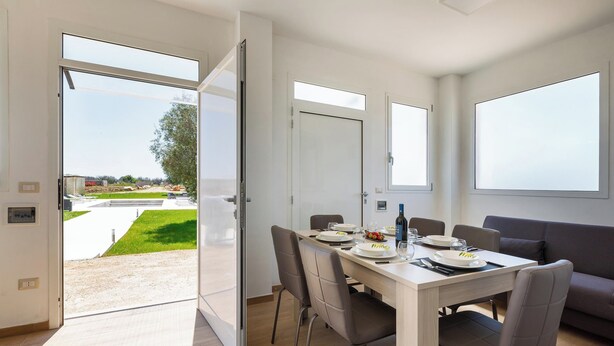 Un espace de restauration moderne avec une table dressée pour quatre personnes, de grandes fenêtres et une vue sur un jardin aménagé à l’extérieur.
